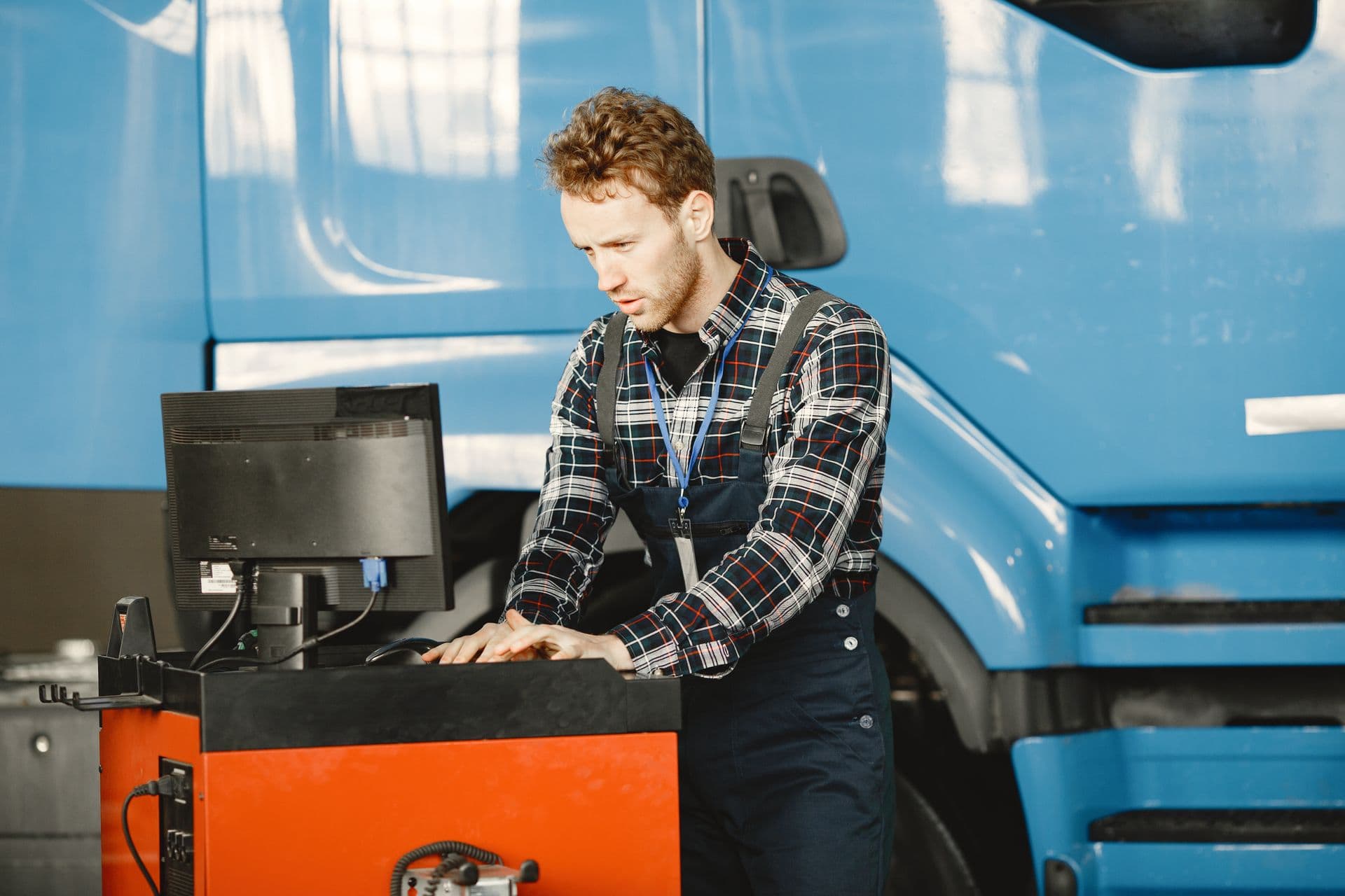 A mechanic in coveralls at the shop computer next to a truck in a service bay.