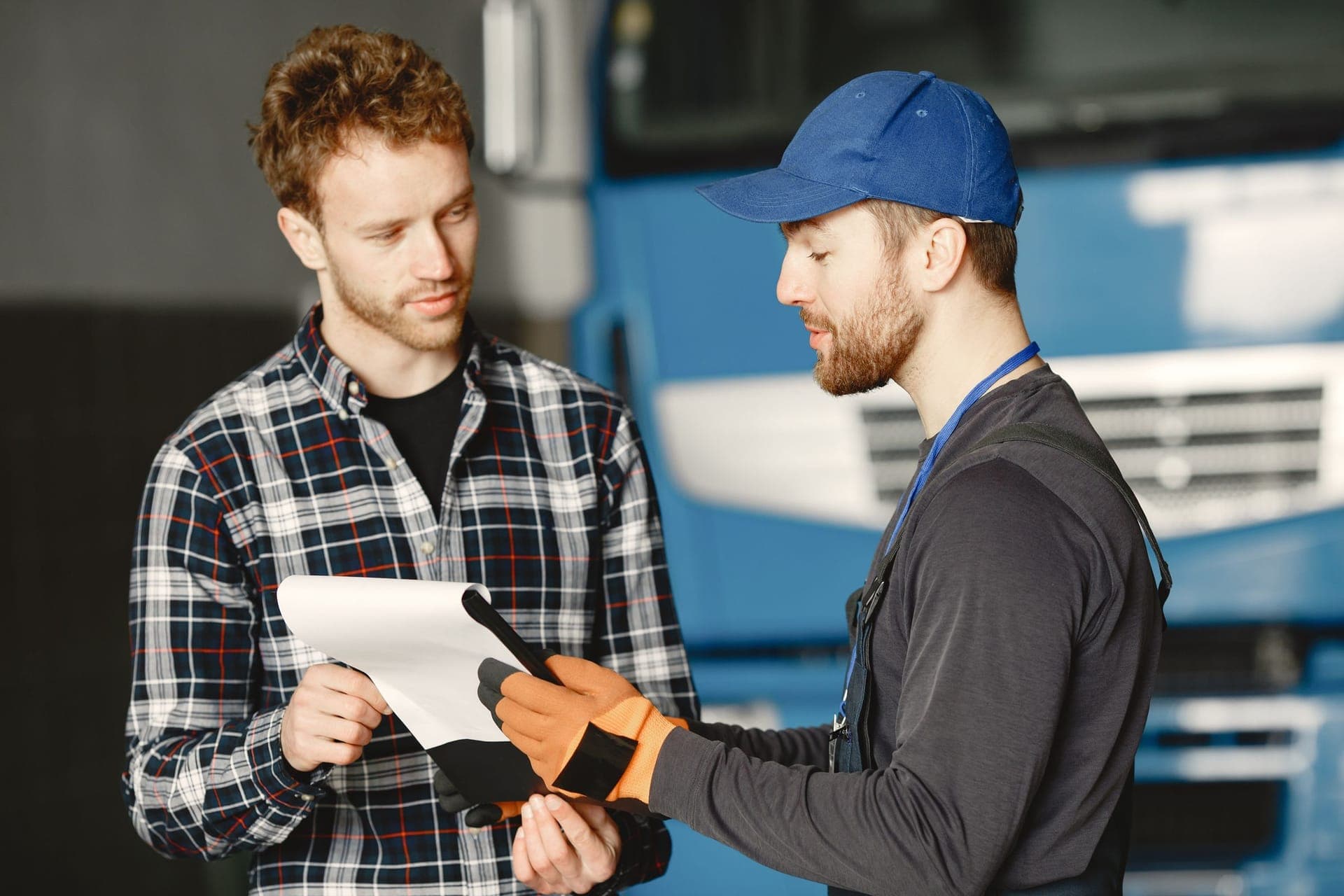 A service technician in workwear going over a written estimate on a clipboard with a customer in a shop bay.