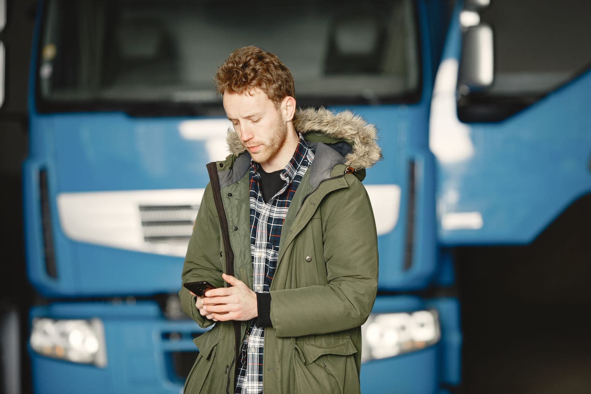 A tradesman in work clothes texting on his phone beside his truck between jobs.